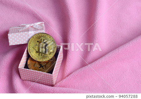 The golden bitcoin lies in a small pink gift box with a small bow on a blanket made of soft and fluffy light pink fleece fabric with a large number of relief folds The golden bitcoin lies in a small pink gift box with a small bow on a blanket made of soft and fluffy light pink fleece fabric with a large number of relief folds 94057288