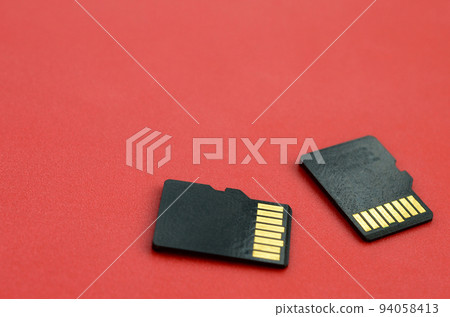 Two small micro SD memory cards lie on a red background. A small and compact data and information store 94058413