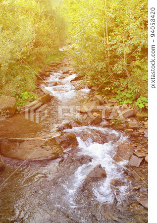 Close-up image of a small wild waterfall in the form of short streams of water between mountain stones 94058420