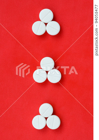 Several white tablets lie on a bright red background in the form of three triangular arrows. Background image on medicine and pharmaceutical topics 94058477