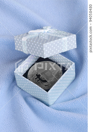 The silver bitcoin lies in a small blue gift box with a small bow on a blanket made of soft and fluffy light blue fleece fabric with a large number of relief folds The silver bitcoin lies in a small blue gift box with a small bow on a blanket made of soft and fluffy light blue fleece fabric with a large number of relief folds 94058480