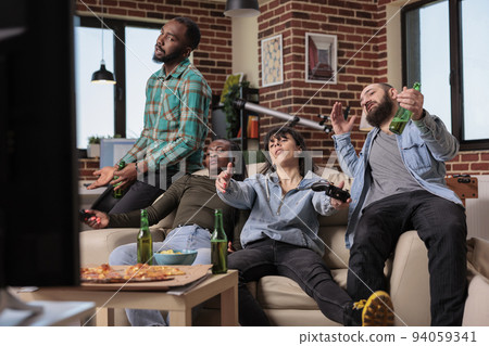 Competitive group of people losing video games play on tv console, feeling sad and frustrated about lost game play. Friends lose competition at house party or gathering, entertainment. 94059341
