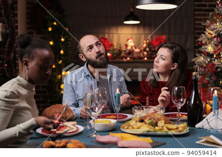 Friends chatting at christmas home party, couple talking at festive dinner table, diverse people eating traditional xmas food. Man and woman having conversation, celebration winter holiday Friends chatting at christmas home party, couple talking at festive dinner table, diverse people eating traditional xmas food. Man and woman having conversation, celebration winter holiday 94059414