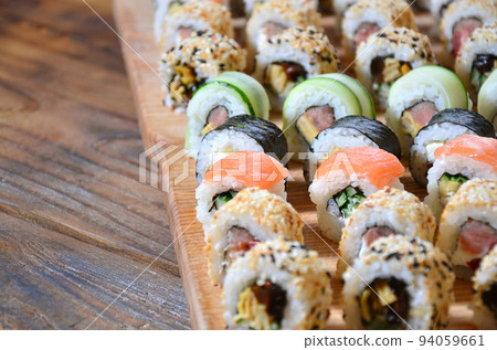 Sushi set of a number of rolls is located on a wooden cutting board on a table in the kitchen of a sushi bar. A traditional dish of oriental cuisine 94059661