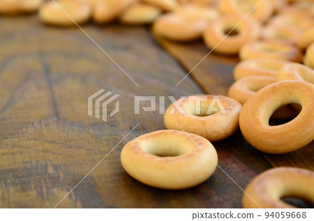 A lot of fresh yellow bagels lie on the surface of the old dark wood. A popular kind of flour products. One of the traditional Russian treats for tea 94059668