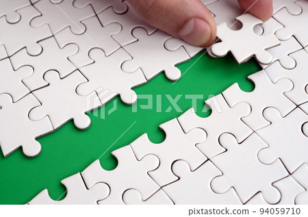 The human hand paves the way to the surface of the jigsaw puzzle, forming a green space. The concept of overcoming the difficulties on the way to success 94059710