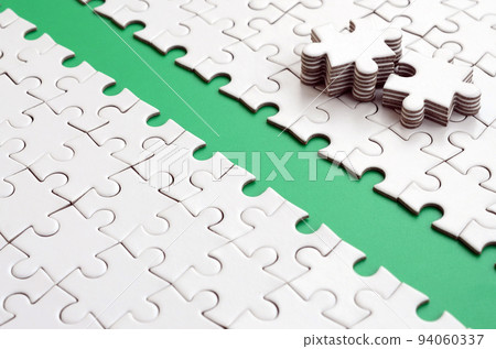 The green path is laid on the platform of a white folded jigsaw puzzle. The missing elements of the puzzle are stacked nearby. Texture image with space for text The green path is laid on the platform of a white folded jigsaw puzzle. The missing elements of the puzzle are stacked nearby. Texture image with space for text 94060337