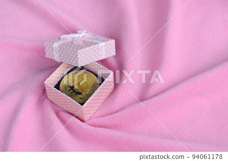 The golden bitcoin lies in a small pink gift box with a small bow on a blanket made of soft and fluffy light pink fleece fabric with a large number of relief folds The golden bitcoin lies in a small pink gift box with a small bow on a blanket made of soft and fluffy light pink fleece fabric with a large number of relief folds 94061178