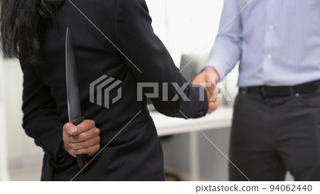 Back view of businesswoman shaking hands with a knife behind his back. Back view of businesswoman shaking hands with a knife behind his back. 94062440