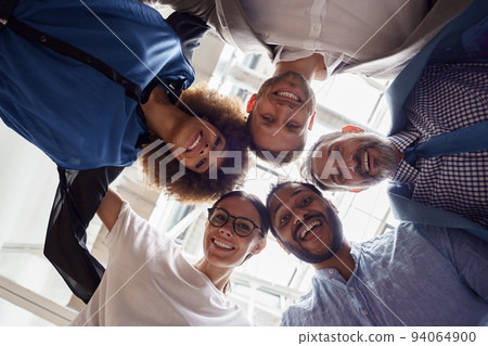 Below view of several happy business partners looking at camera while embracing each other Below view of several happy business partners looking at camera while embracing each other 94064900
