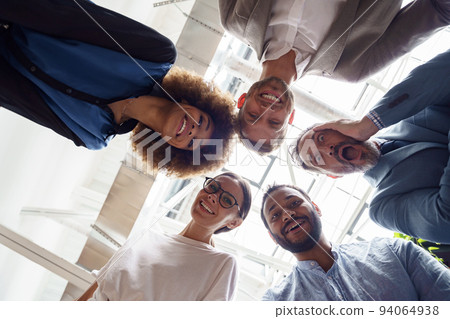 Below view of several happy business partners looking at camera while embracing each other Below view of several happy business partners looking at camera while embracing each other 94064938