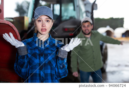 Upset young workwoman standing near tractor in farm backyard 94066724