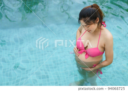 happy pregnant woman in bikini looking her belly in swimming pool 94068725