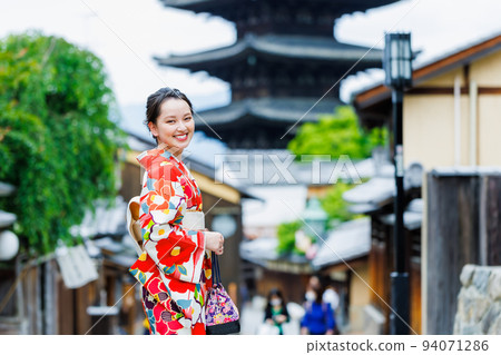 A young woman in a kimono standing with a five-storied pagoda in the background 94071286