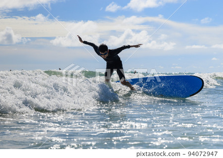 Young boy, new student in surfing, loses his body balance and falls from surfboard into the water during class. Young boy, new student in surfing, loses his body balance and falls from surfboard into the water during class. 94072947