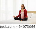 Pregnant woman sits in bed in her bedroom meditating alone in peace and happiness. The new mother resting by sitting down to chill out. 94073066
