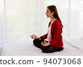 Pregnant woman sits in bed in her bedroom meditating alone in peace and happiness. The new mother resting by sitting down to chill out. 94073068