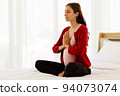 Pregnant woman sits in bed in her bedroom meditating alone in peace and happiness. The new mother resting by sitting down to chill out. 94073074