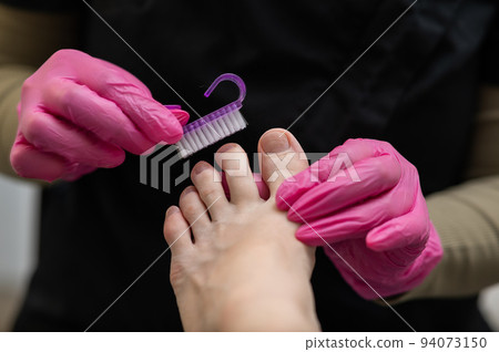 Pedicure master cleans client's toes from nail dust with a brush. Pedicure master cleans client's toes from nail dust with a brush. 94073150