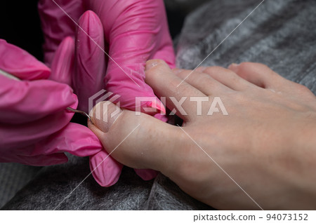 Podiatrist makes a pedicure to a client. The master conducts hygiene of the toes with a metal stick. 94073152