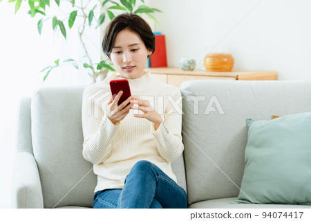 觀看在沙發的婦女一個智能手機 94074417
