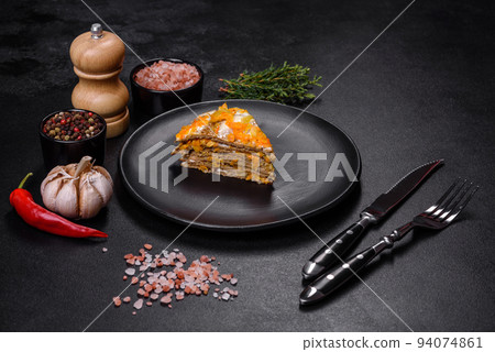 Delicious fresh liver cake with mayonnaise and carrots on a black plate against a dark concrete background 94074861