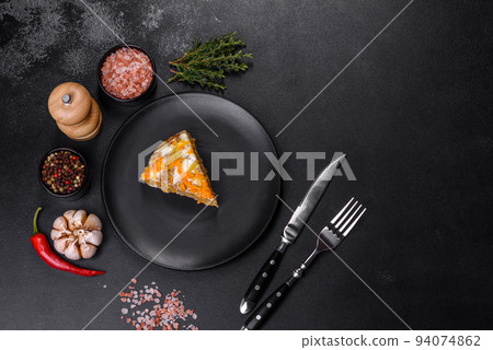Delicious fresh liver cake with mayonnaise and carrots on a black plate against a dark concrete background 94074862