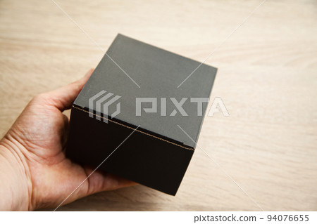 Closed rectangular cardboard box with corrugated cardboard lid and hand on oak wooden table 94076655