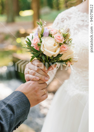 The groom holds out a wedding bouquet to the bride. Close-up of newlywed hands and delicate bouquet 94079622