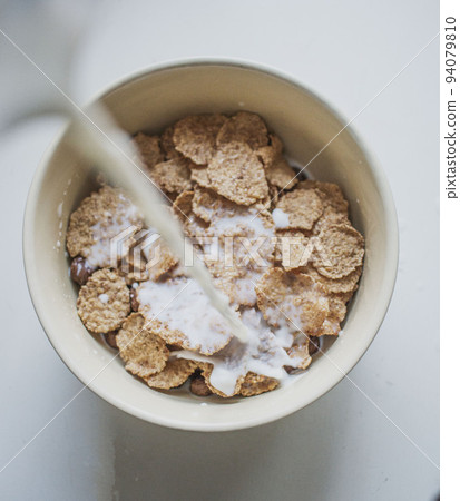 pouring milk into a white bowl with corn flakes, top view 94079810