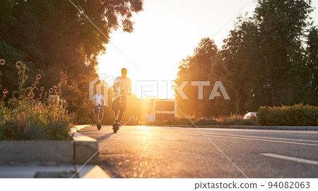 Mans are riding on electric scooters or e-scooters on the street on the sunset. Mans are riding on electric scooters or e-scooters on the street on the sunset. 94082063