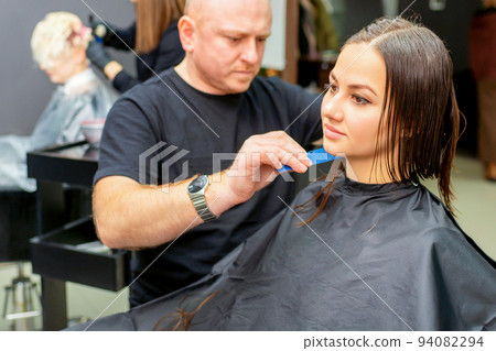 Haircut of long wet hair of young caucasian woman by a male hairdresser in a hair salon 94082294
