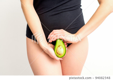 Healthy nutrition and pregnancy concept. Young woman holding one half of an avocado fruit close to her belly over a white background Healthy nutrition and pregnancy concept. Young woman holding one half of an avocado fruit close to her belly over a white background 94082348