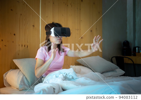 Young woman using virtual reality headset in bed. VR, Future digital technology, game, movies entertainment, metaverse, NFT and 3D cyberspace concept 94083112