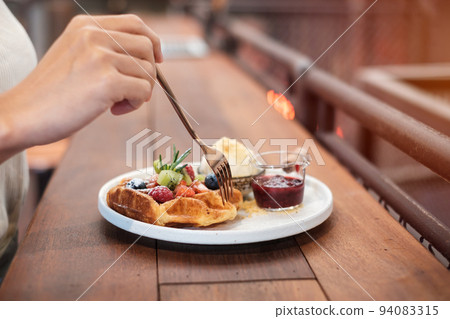 Woman eating dessert with fresh berries and fruit at cafe 94083315