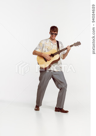 Portrait of young ma in sunglasses and vinatge clothes playing guitar, posing isolated over white studio background Portrait of young ma in sunglasses and vinatge clothes playing guitar, posing isolated over white studio background 94084689