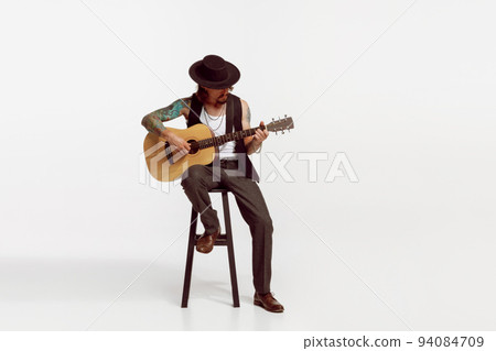 Portrait of stylish man, rock musician playing guitar, performing isolated over white studio background Portrait of stylish man, rock musician playing guitar, performing isolated over white studio background 94084709