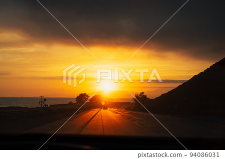 Stunning golden orange sunset on highway 101 California with few cars ocean and mountains. Road trip west coast USA 94086031