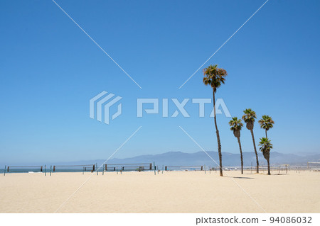 Green Palm trees and volleyball nets on Venice beach Los Angeles California on a bright sunny day against blue sky no people Green Palm trees and volleyball nets on Venice beach Los Angeles California on a bright sunny day against blue sky no people 94086032