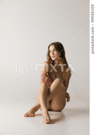 Studio shot of young charming slim girl in grey cotton underwear isolated over gray background. Wellness, fitness, diet, fashion, natural beauty of female body Studio shot of young charming slim girl in grey cotton underwear isolated over gray background. Wellness, fitness, diet, fashion, natural beauty of female body 94088109