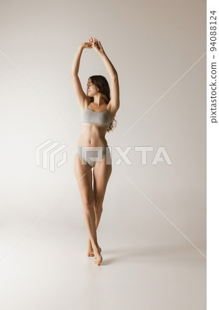 Studio shot of young charming slim girl in grey cotton underwear isolated over gray background. Wellness, fitness, diet, fashion, natural beauty of female body Studio shot of young charming slim girl in grey cotton underwear isolated over gray background. Wellness, fitness, diet, fashion, natural beauty of female body 94088124