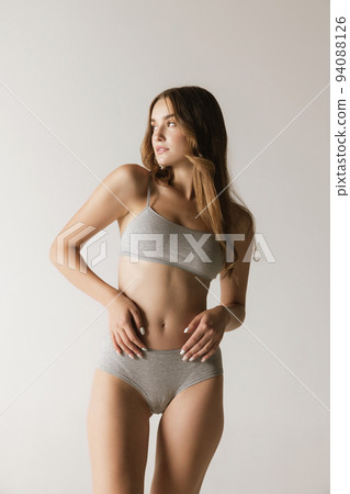 Studio shot of young charming slim girl in grey cotton underwear isolated over gray background. Wellness, fitness, diet, fashion, natural beauty of female body Studio shot of young charming slim girl in grey cotton underwear isolated over gray background. Wellness, fitness, diet, fashion, natural beauty of female body 94088126