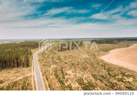 Aerial view of highway road through deforestation area landscape. Green pine forest in deforestation zone. Top view of field and forest landscape in sunny spring day. Drone view. Bird's eye view 94089110