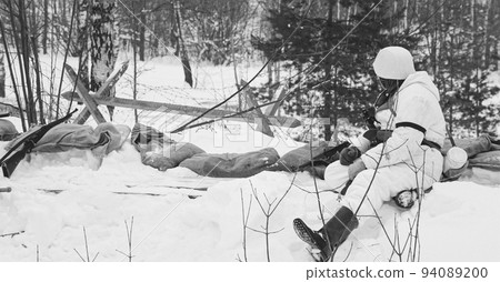 Hidden Re-enactor Dressed As German Wehrmacht Infantry Soldier In World War II Soldiers Sitting In Ambush In Winter Forest. Historical Re-enactment. WWII. Winter Snowy Day. Black And White Photo 94089200