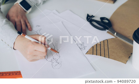Close-up of fashion designer is drawing lines on clothing sketch. Woman is busy and concentrated on work. 94089720
