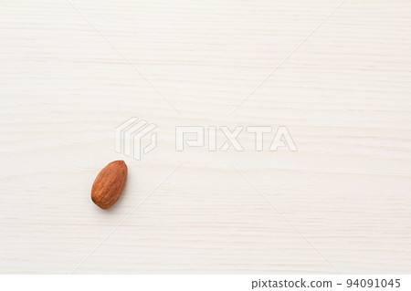 A single almond on a light wood grain table seen from an overhead angle 94091045