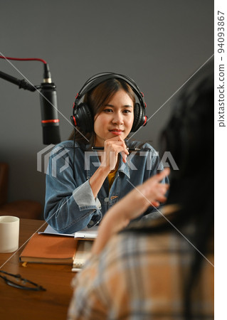 Positive female radio host listening to interesting conversation with guest during recording podcast in broadcasting home studio Positive female radio host listening to interesting conversation with guest during recording podcast in broadcasting home studio 94093867