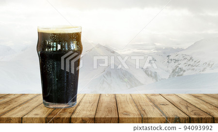 Winter drinks. Large glass of dark frothy beer standing on wooden table over snow-capped mountains background. 94093992