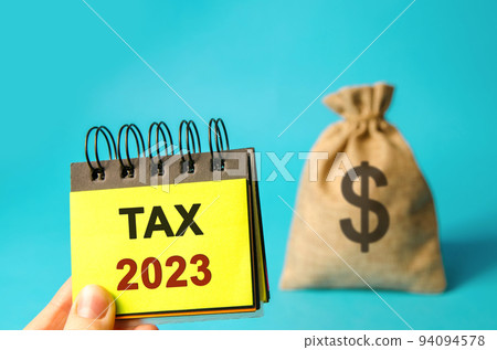 Notes with word Taxes 2023 and money bag. The concept of paying the tax rate. Taxation, taxes burden. Pay off debts. Property income annual taxes 94094578