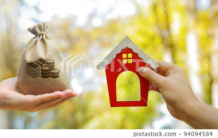 Miniature wooden house and money bag in the hands of a man outdoors. Real estate concept. Eco-friendly home. Buying a housing outside the city. Red roof. Selective focus 94094584